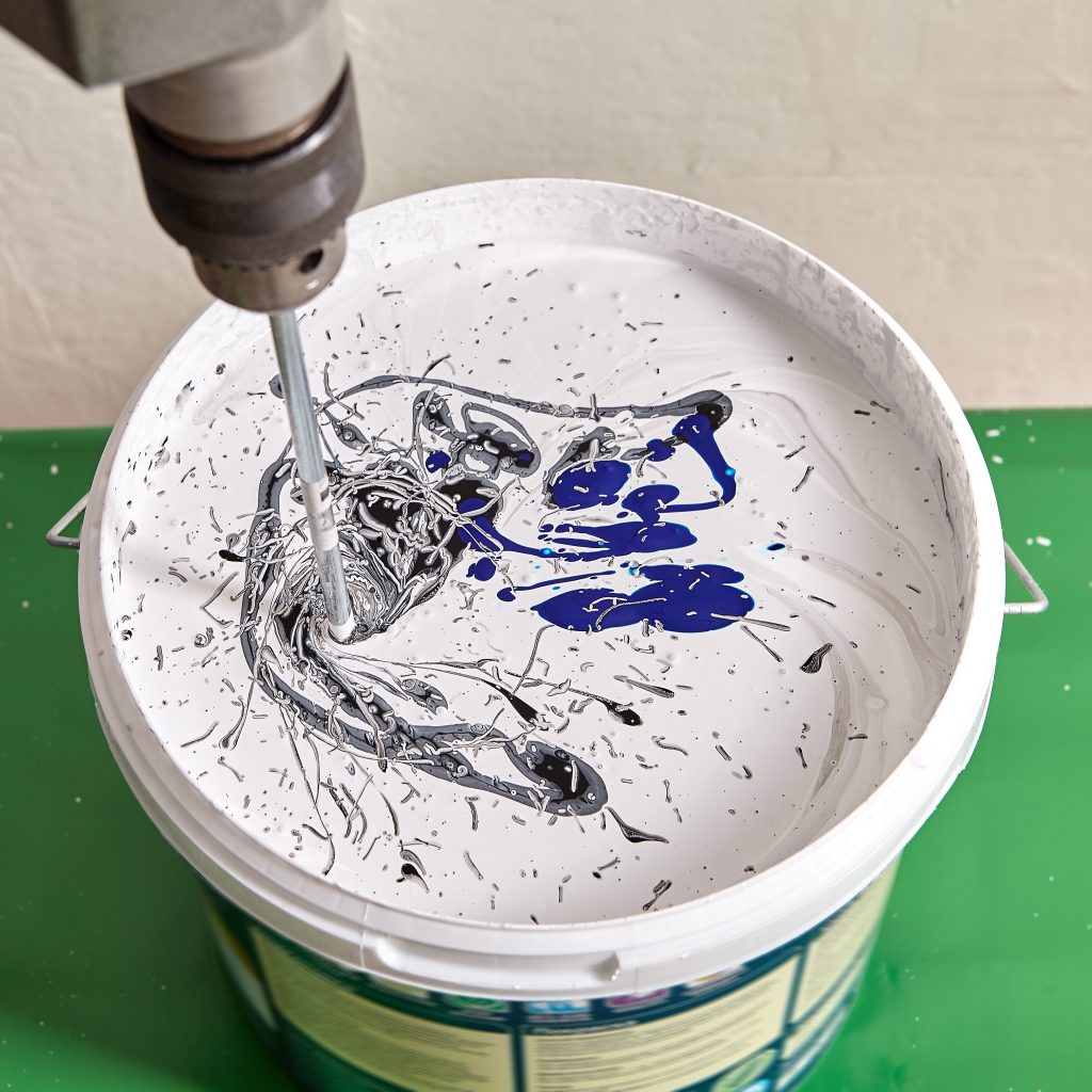 Paint mixing with paddle whisk. The painter tints the dye in a bucket for painting walls during renovation in the flat.